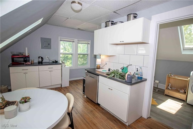 kitchen featuring white cabinets, dishwasher, light hardwood / wood-style floors, tasteful backsplash, and vaulted ceiling with skylight