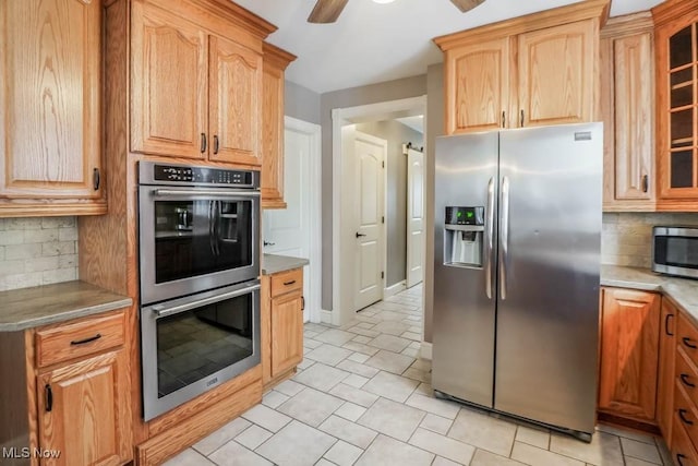 kitchen featuring appliances with stainless steel finishes, light tile patterned floors, ceiling fan, light stone counters, and decorative backsplash