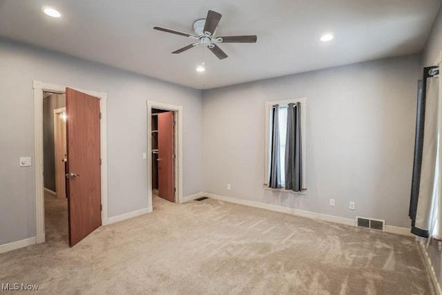 unfurnished bedroom with ceiling fan, a walk in closet, a closet, and light carpet