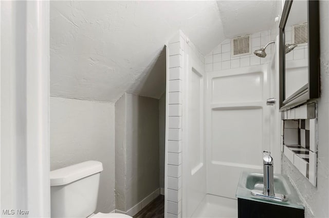 bathroom with lofted ceiling, a shower, and toilet