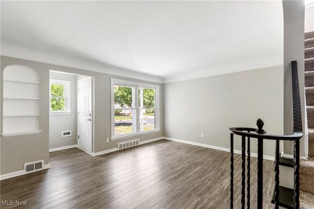 unfurnished room featuring built in shelves and dark hardwood / wood-style floors