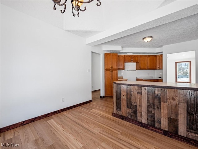 kitchen featuring a textured ceiling, light wood-type flooring, a notable chandelier, and kitchen peninsula