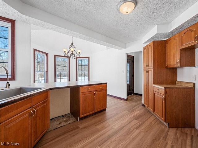 kitchen featuring a chandelier, kitchen peninsula, a textured ceiling, sink, and decorative light fixtures