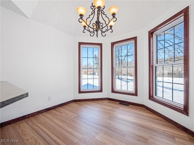 unfurnished dining area with a notable chandelier, light hardwood / wood-style flooring, a wealth of natural light, and a textured ceiling