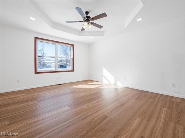 unfurnished room featuring a raised ceiling, ceiling fan, and light hardwood / wood-style floors