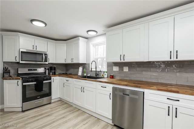 kitchen with appliances with stainless steel finishes, white cabinetry, butcher block countertops, and sink