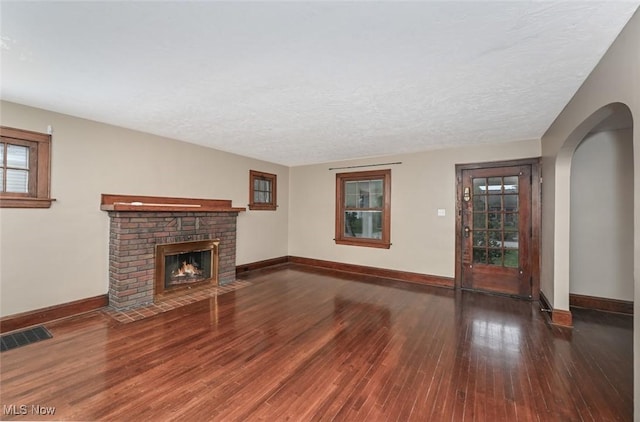 unfurnished living room featuring a brick fireplace, dark wood-type flooring, and a textured ceiling