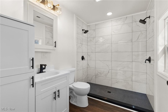 bathroom featuring toilet, wood-type flooring, vanity, and tiled shower