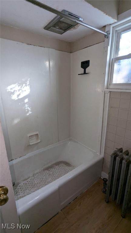 bathroom with bathtub / shower combination, radiator heating unit, and hardwood / wood-style floors