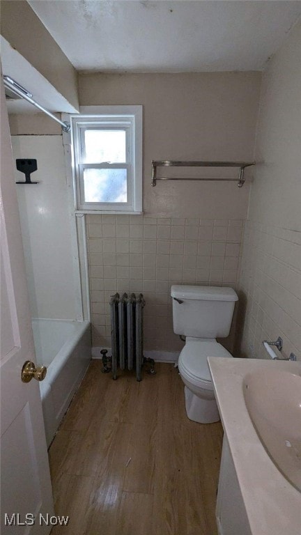 full bathroom with tile walls, tub / shower combination, radiator, wood-type flooring, and toilet