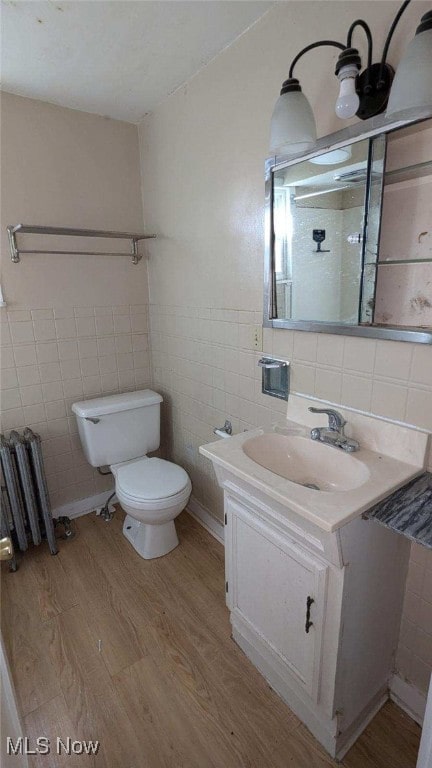 bathroom with hardwood / wood-style floors, toilet, vanity, radiator, and tile walls