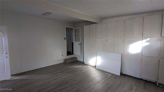 spare room featuring beam ceiling and dark wood-type flooring