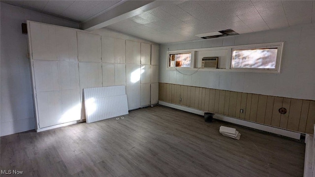 interior space with wood-type flooring, wood walls, a baseboard radiator, lofted ceiling with beams, and a wall mounted air conditioner