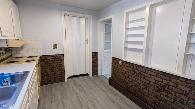 kitchen with white cabinets, light wood-type flooring, brick wall, and sink