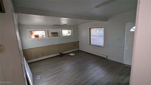 empty room with beam ceiling, a wall mounted air conditioner, wood walls, and hardwood / wood-style flooring