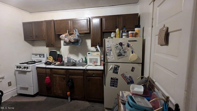 kitchen with white appliances, dark brown cabinetry, and sink