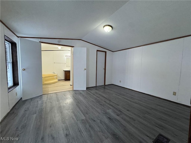 unfurnished bedroom with ensuite bath, vaulted ceiling, and hardwood / wood-style floors