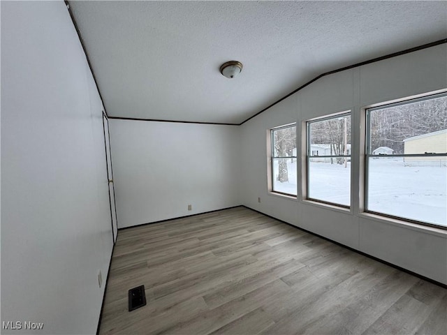 unfurnished room with vaulted ceiling, plenty of natural light, and light hardwood / wood-style flooring