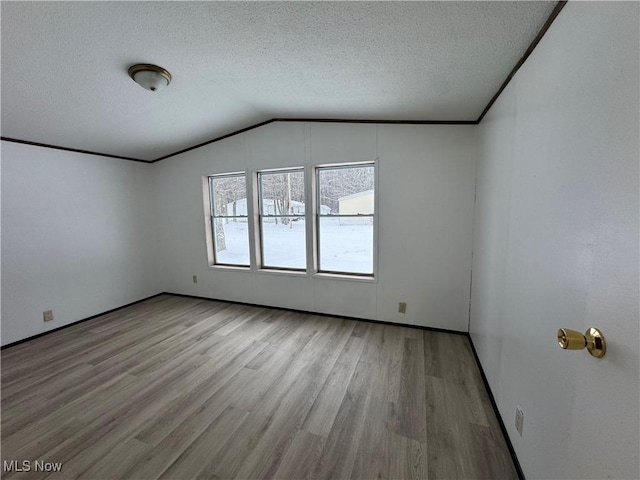 unfurnished room with light hardwood / wood-style floors, vaulted ceiling, and a textured ceiling