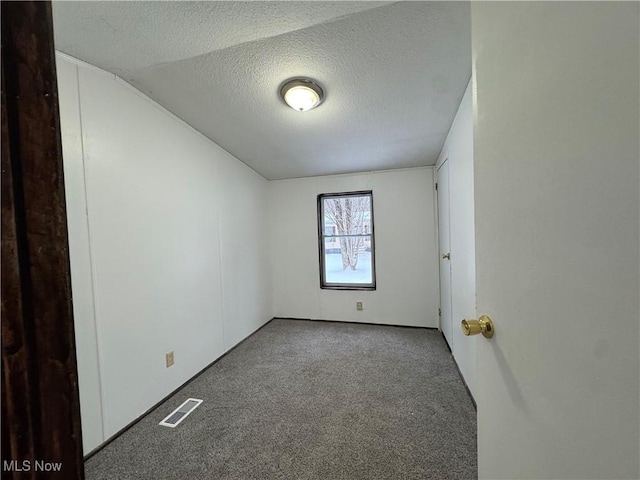 unfurnished room with a textured ceiling, vaulted ceiling, and carpet flooring