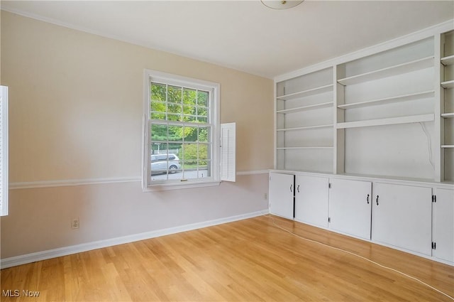 unfurnished room featuring built in shelves and light hardwood / wood-style floors