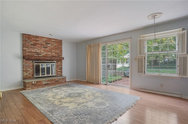 unfurnished living room with a brick fireplace, baseboard heating, a healthy amount of sunlight, and light wood-type flooring