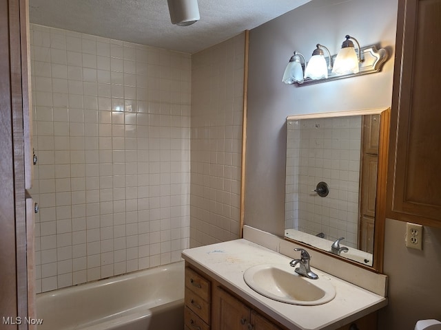 bathroom with a textured ceiling, tiled shower / bath, and vanity