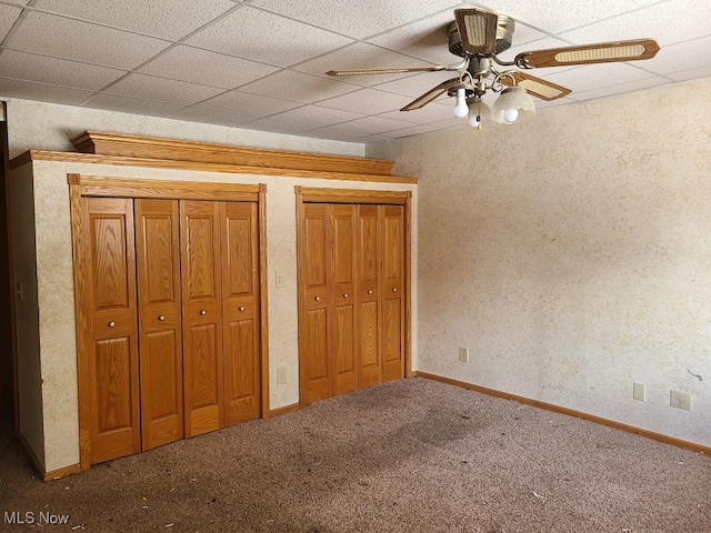 unfurnished bedroom featuring a paneled ceiling, ceiling fan, carpet flooring, and multiple closets