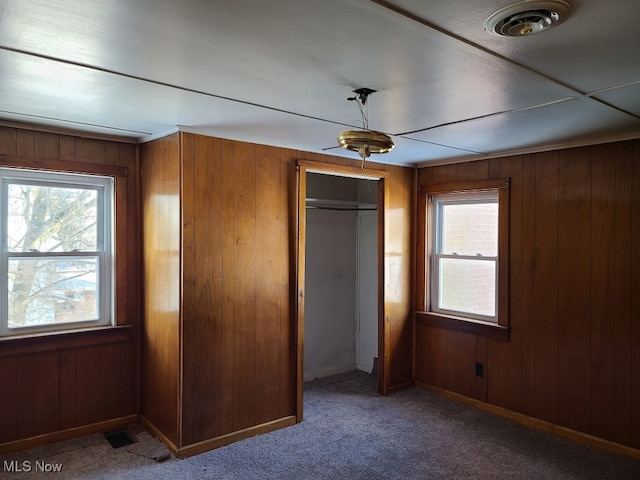 unfurnished bedroom with wood walls, ceiling fan, a closet, and carpet