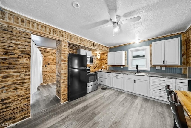 kitchen featuring white cabinets, sink, wooden walls, and stainless steel appliances