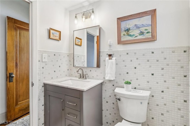 bathroom with toilet, vanity, and tile walls