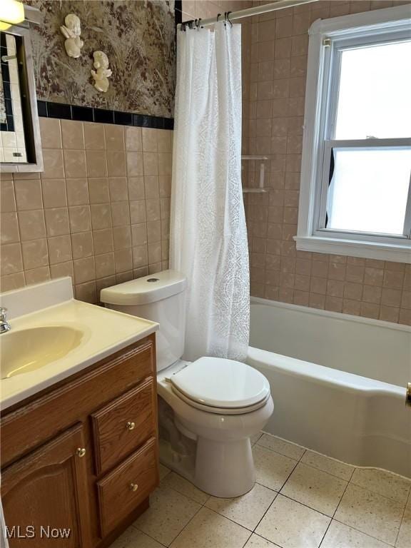 full bathroom featuring toilet, vanity, tile patterned floors, tile walls, and shower / tub combo with curtain