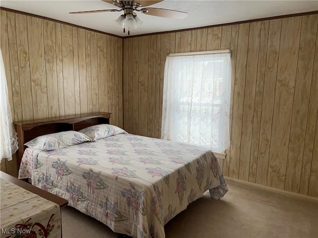 carpeted bedroom featuring wood walls, ceiling fan, and ornamental molding