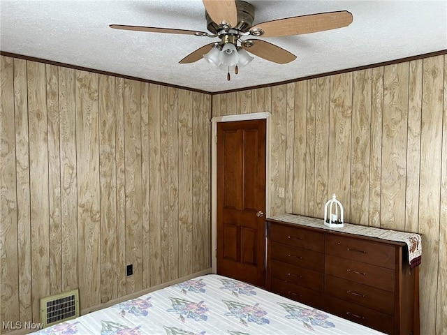 unfurnished bedroom with wooden walls, a textured ceiling, ceiling fan, and crown molding