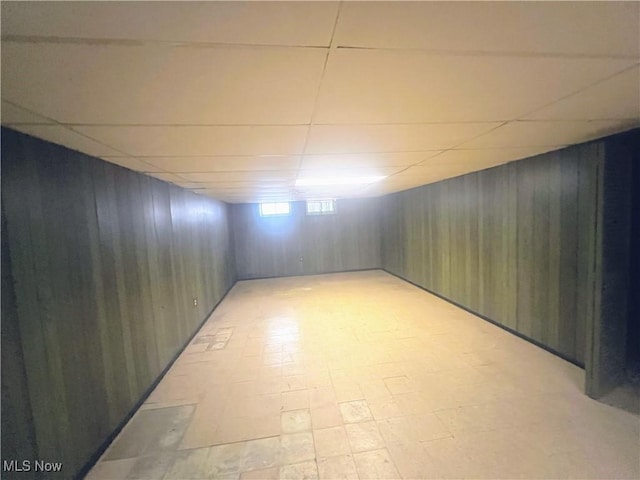 basement featuring wood walls and a drop ceiling