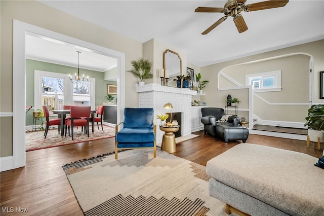 living room with ceiling fan with notable chandelier, wood-type flooring, and a fireplace