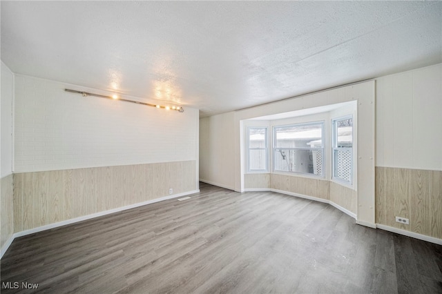 empty room featuring wooden walls, a textured ceiling, and hardwood / wood-style floors