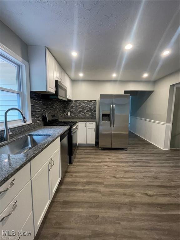 kitchen featuring stainless steel appliances, sink, white cabinetry, dark stone countertops, and dark hardwood / wood-style flooring