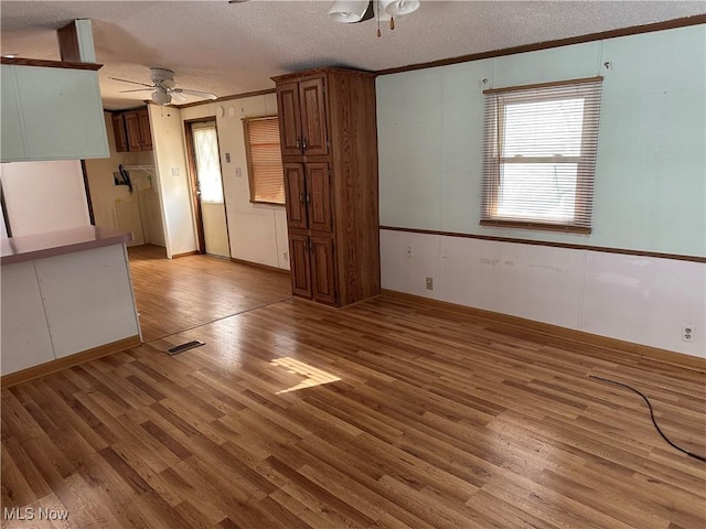 unfurnished living room featuring a textured ceiling, ceiling fan, ornamental molding, and light hardwood / wood-style flooring