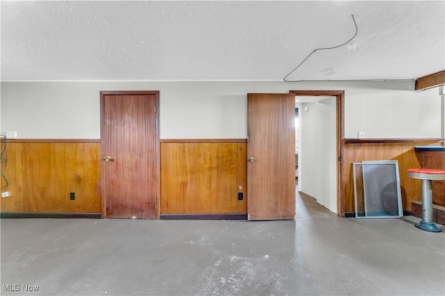 empty room featuring a textured ceiling, wood walls, and concrete floors