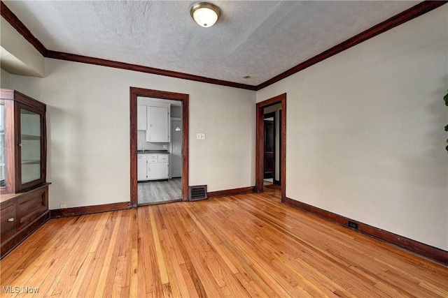 spare room with ornamental molding, a textured ceiling, and light wood-type flooring