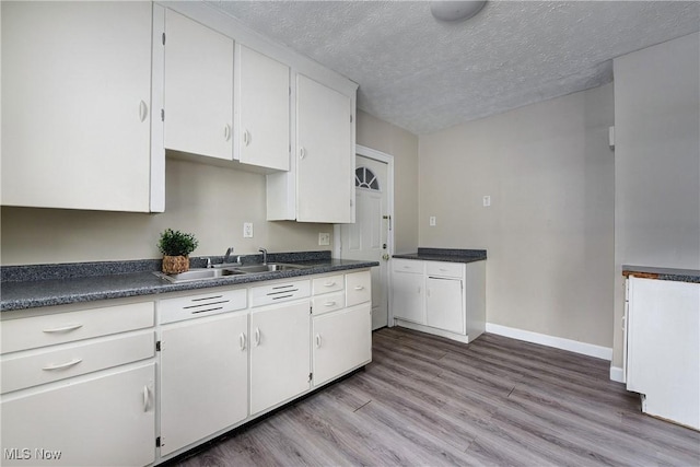 kitchen featuring sink, white cabinetry, light wood-type flooring, and a textured ceiling