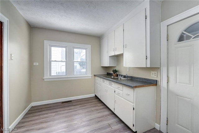 kitchen featuring white cabinets, a textured ceiling, light hardwood / wood-style floors, and sink