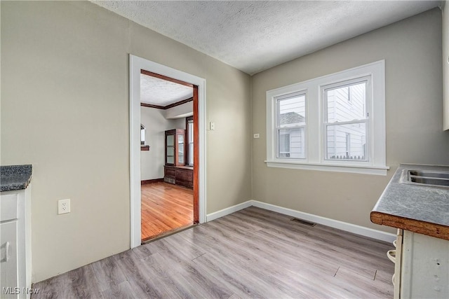 unfurnished dining area featuring a textured ceiling, light wood-type flooring, and sink