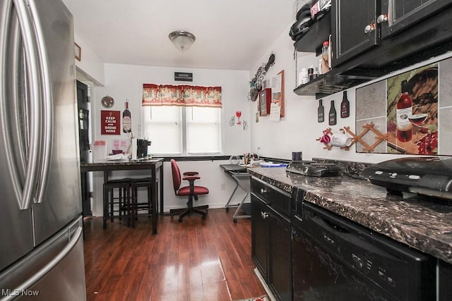 kitchen featuring dark wood-type flooring, stainless steel fridge, and dark stone countertops