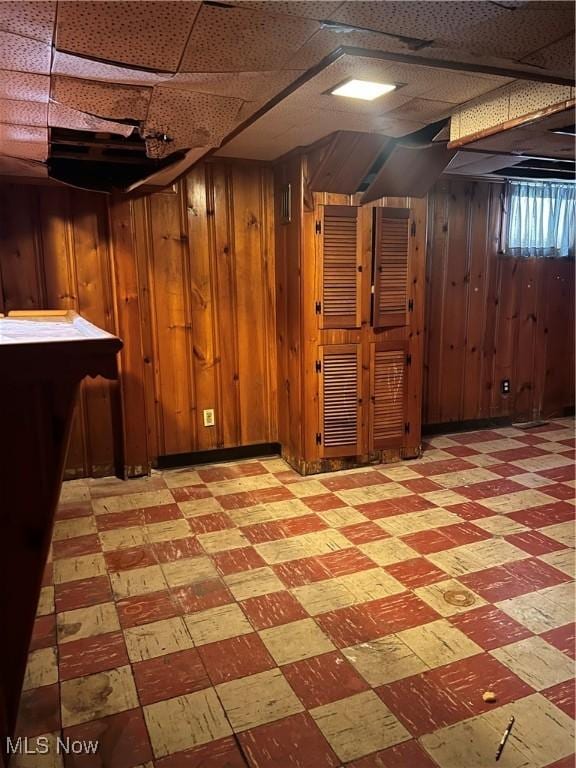 basement with indoor bar, a drop ceiling, and wooden walls