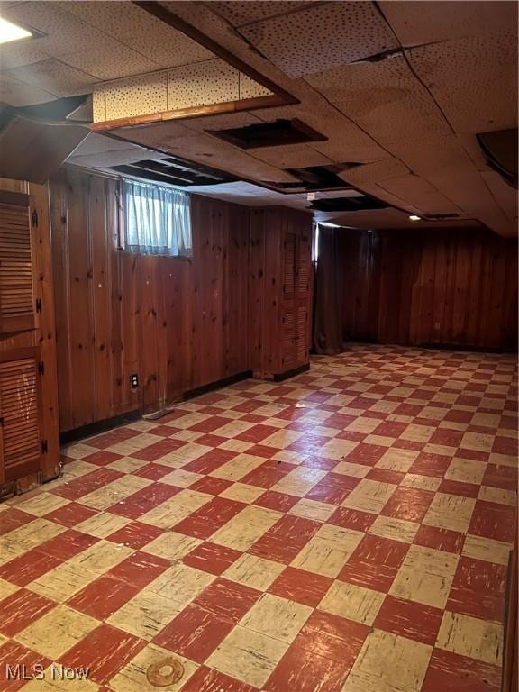 basement with a paneled ceiling and wooden walls