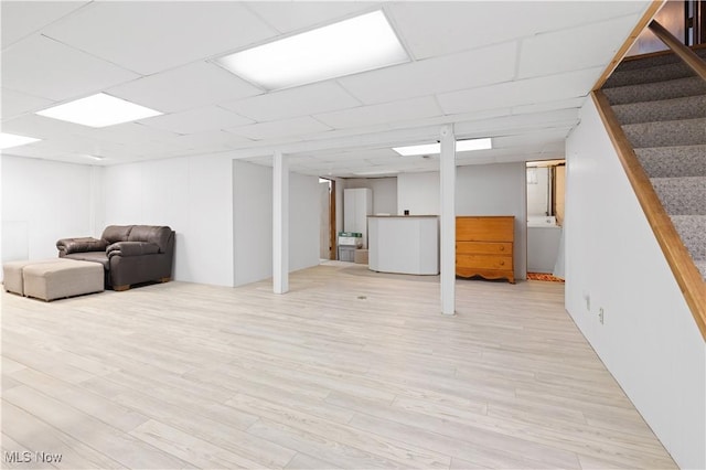 basement with a paneled ceiling and light wood-type flooring