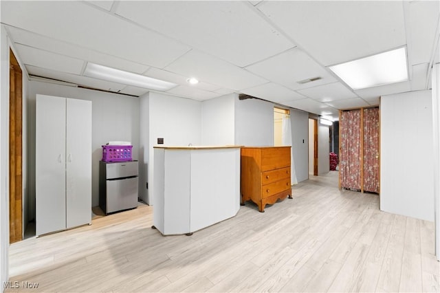 basement featuring stainless steel fridge and light hardwood / wood-style flooring