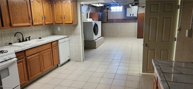 kitchen featuring sink, light tile patterned floors, tile counters, white appliances, and washer and clothes dryer